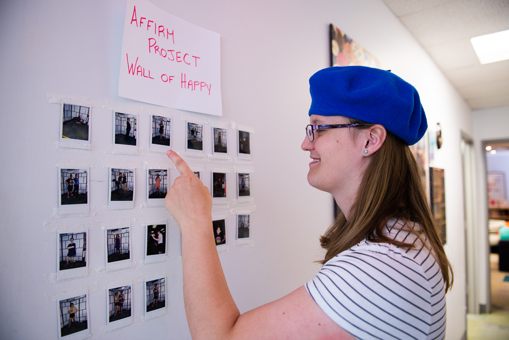 Penelope next to the ‘Wall of Happy’, pointing at a photo of her in her new clothes, thanks to Affirm Project.